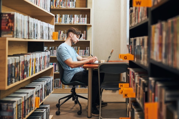 Uczeń uczący się w bibliotece młody człowiek przygotowujący się do egzaminu na laptopie człowiek słuchający kursu online